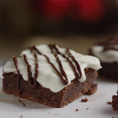 Photograph of a chocolate brownie square with white frosting and chocolate drizzle