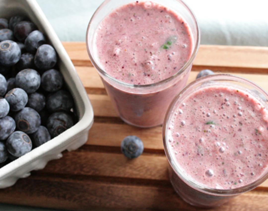 Licuadora con frutas y verduras verdes sobre un fondo claro. preparación de  un batido saludable. la mano pone un trozo de manzana en el bol de la  batidora.