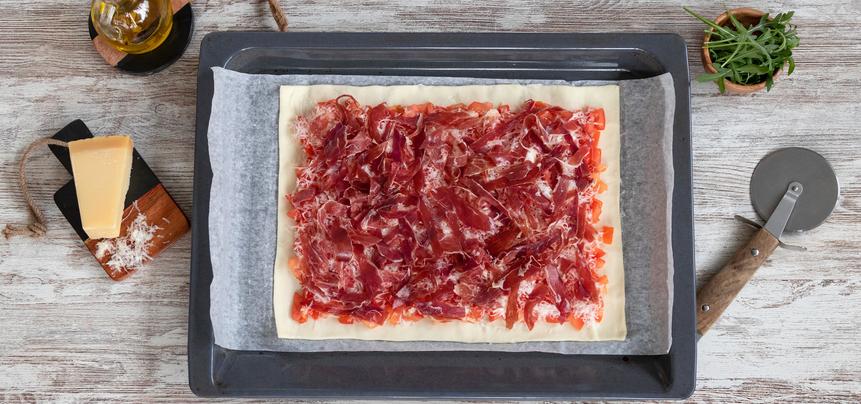 Pizza de jamón ibérico y tomate con rúcula y parmesano