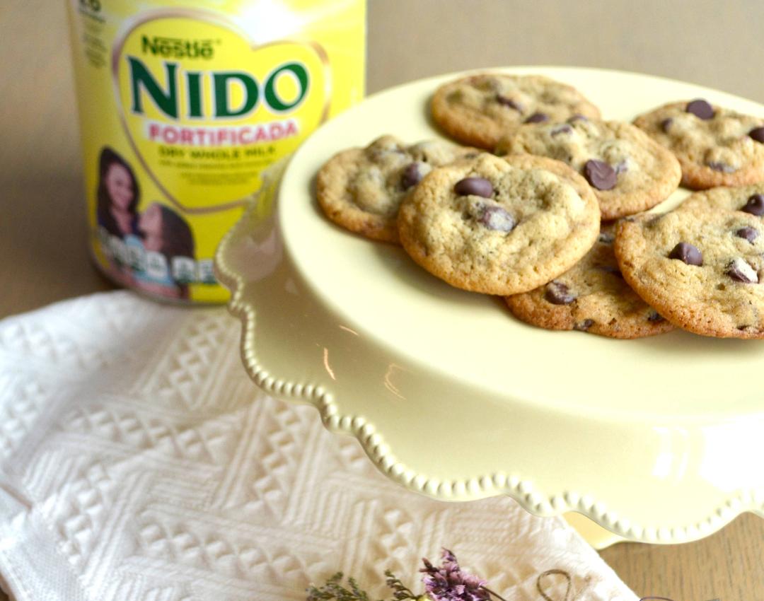 NIDO® x NESTLÉ® TOLL HOUSE® Chocolate Chip Cookies with semi-sweet morsels, baked golden, on a white plate.