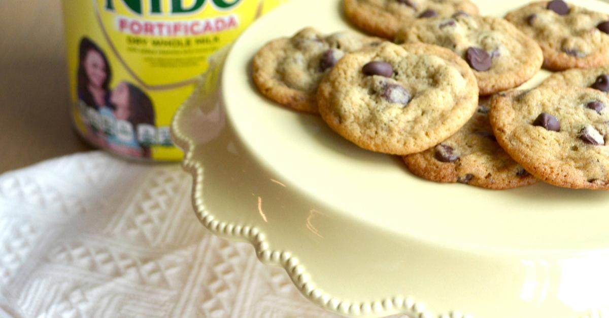 NIDO® x NESTLÉ® TOLL HOUSE® Chocolate Chip Cookies with semi-sweet morsels, baked to golden perfection on a white plate.