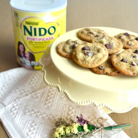 NIDO® x NESTLÉ® TOLL HOUSE® Chocolate Chip Cookies with semi-sweet morsels, baked golden, on a white plate.