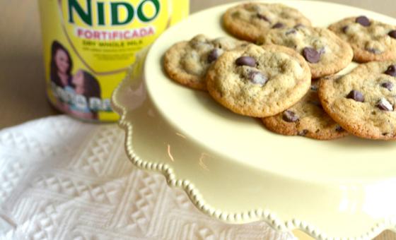 NIDO® x NESTLÉ® TOLL HOUSE® Chocolate Chip Cookies with semi-sweet morsels, baked to golden perfection on a white plate.