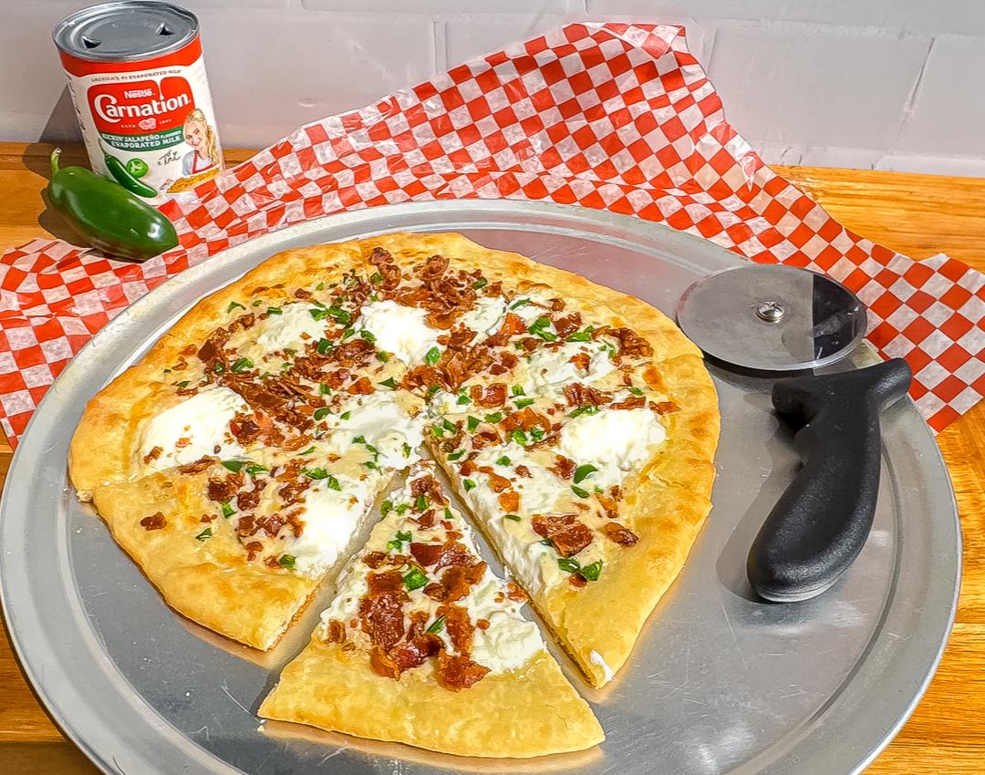 Jalapeño Bacon White Pizza by CARNATION®, topped with bacon, jalapeños, and creamy white sauce with Kickin’ Jalapeño Milk.