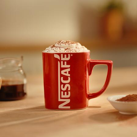 Photograph: red Nescafé mug with frothy, cocoa-topped coffee on a wooden table
