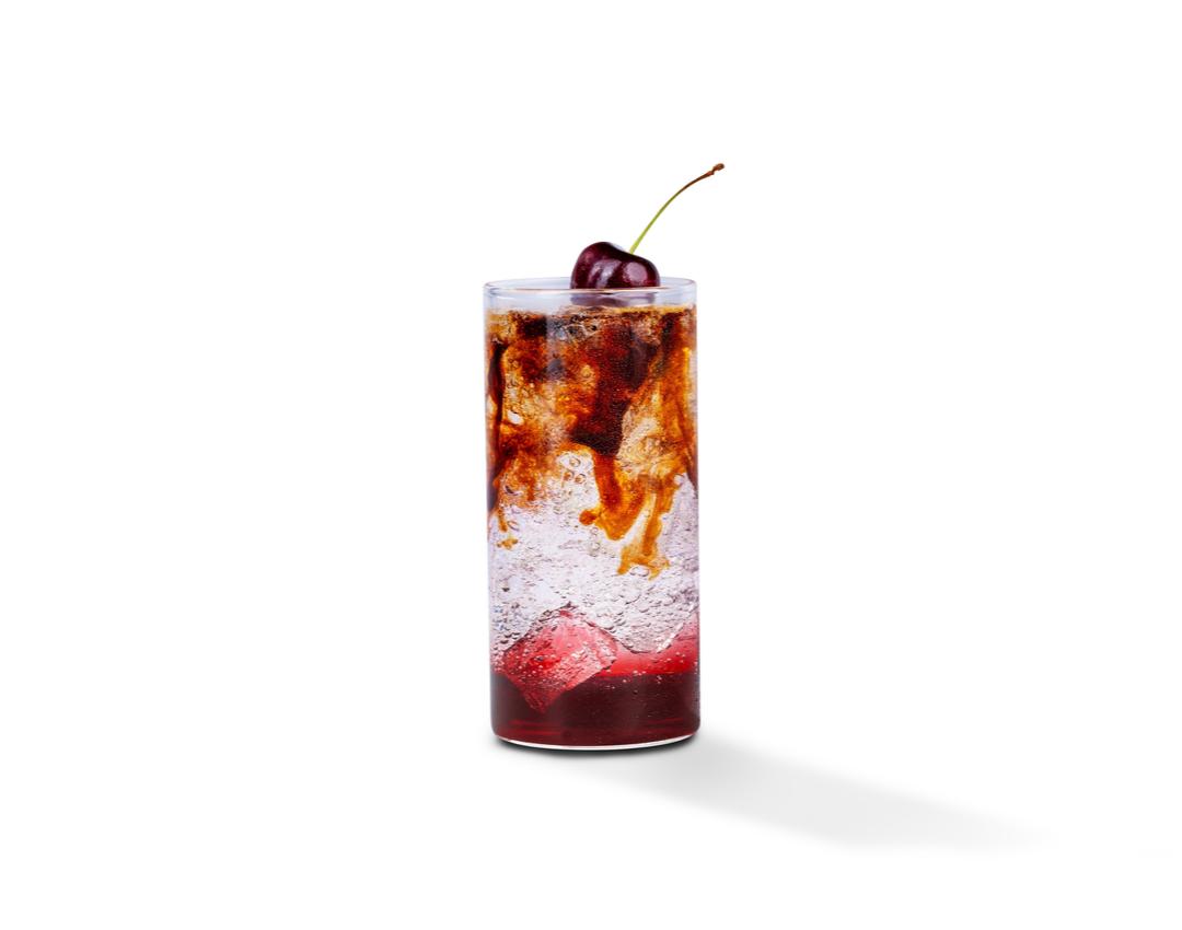 Photograph: tall cocktail glass with cola and cream swirling over ice, cherry garnish