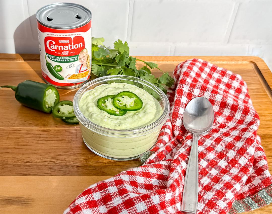 Avocado Crema by CARNATION® MILKS with avocado, jalapeño milk, cilantro, and lime, served in a white bowl on a wooden table.