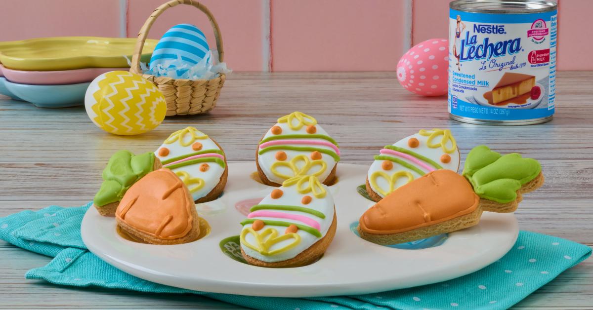 Fotografía: galletas decoradas de Pascua (zanahorias y huevos) sobre plato blanco, fondo pastel