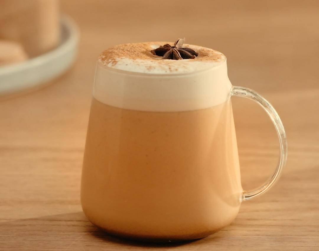 Photograph: glass mug with frothy spiced latte topped with star anise on wood