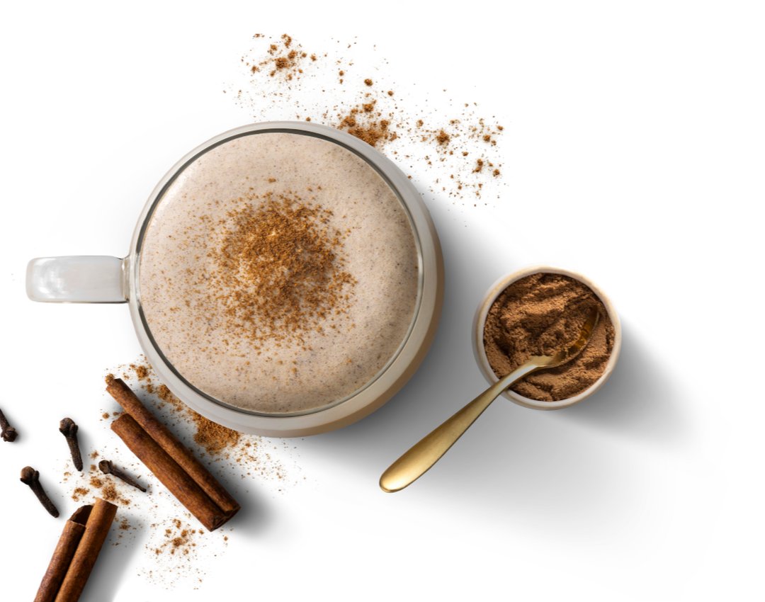 Top-down photograph: frothy cappuccino dusted with cinnamon, spoon of cinnamon, sticks and coffee beans.